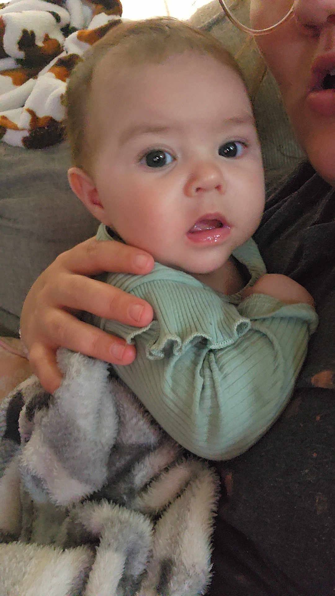 Anna joined the competition — help win amazing prizes! baby, infant, child, blanket, hand, person, face, clothing, indoor, couch, curious, wide_eyes, mint_green, soft_texture, holding, partial_face, close_up, expression, comfortable, warm