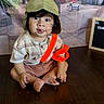 baby, backdrop, child, curly_hair, cute, hat, indoor, person, pilot_hat, playful, portrait, shorts, signboard, sitting, smiling, striped_shirt, toddler, tongue_out, tricycle, wooden_floor