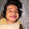 baby, bed, bedding, blanket, child, cute, expression, face, hair, happy, head, indoors, infant, lying_down, person, portrait, skin, smiling, tongue_out, yellow_clothing