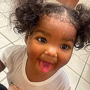 Z'Naya joined the competition — help win amazing prizes! child, toddler, curly_hair, pigtails, tongue_out, smiling, white_shirt, flower_design, indoor, tile_floor, cute, playful, portrait, person, happy, young_child, closeup, funny_face, girl, casual_clothing
