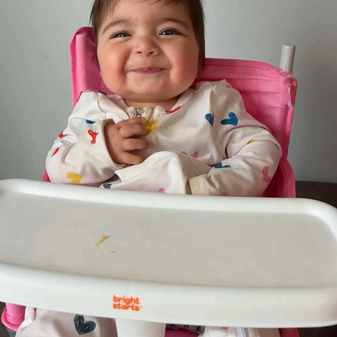 Jasmine is registered to the contest to win money with this photo: baby, child, clothing, cozy, cute, face, food_tray, hair, happy, heart_pattern, high_chair, indoor, joy, person, pink, playful, sitting, smiling, toddler, white