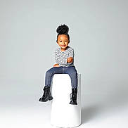 Marley joined the competition — help win amazing prizes! child, smiling, portrait, studio, minimalist, black_bow, striped_shirt, blue_jeans, black_boots, cylindrical_pedestal, high_puff_hairstyle, seated, fashion, happy, casual_clothing, young_kid, isolated_background, cute, modern, confident