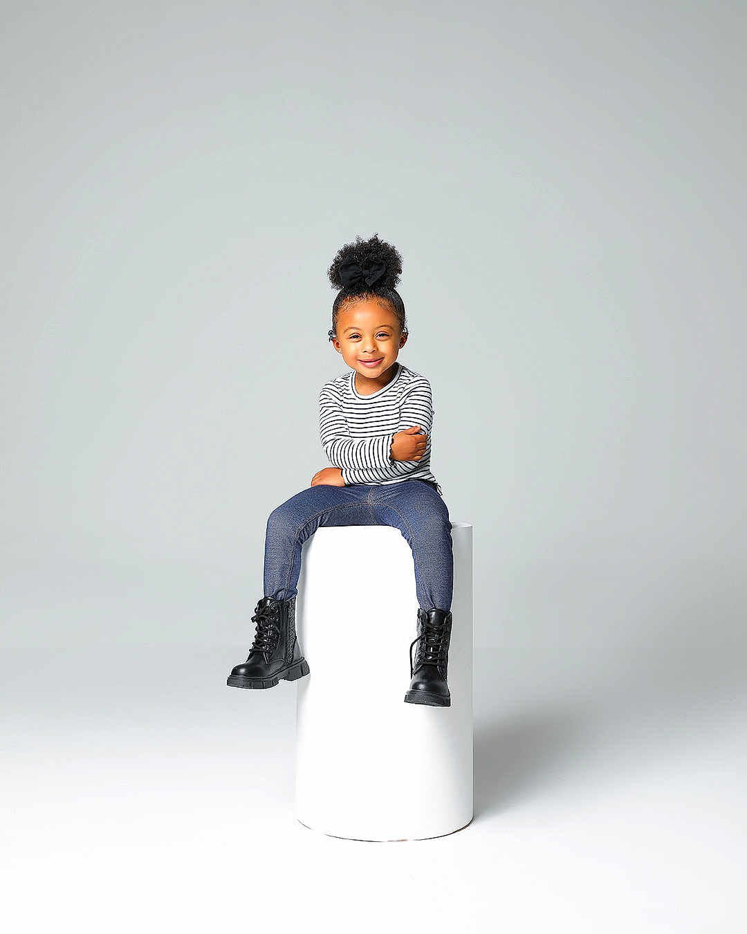 Marley joined the competition — help win amazing prizes! child, smiling, portrait, studio, minimalist, black_bow, striped_shirt, blue_jeans, black_boots, cylindrical_pedestal, high_puff_hairstyle, seated, fashion, happy, casual_clothing, young_kid, isolated_background, cute, modern, confident