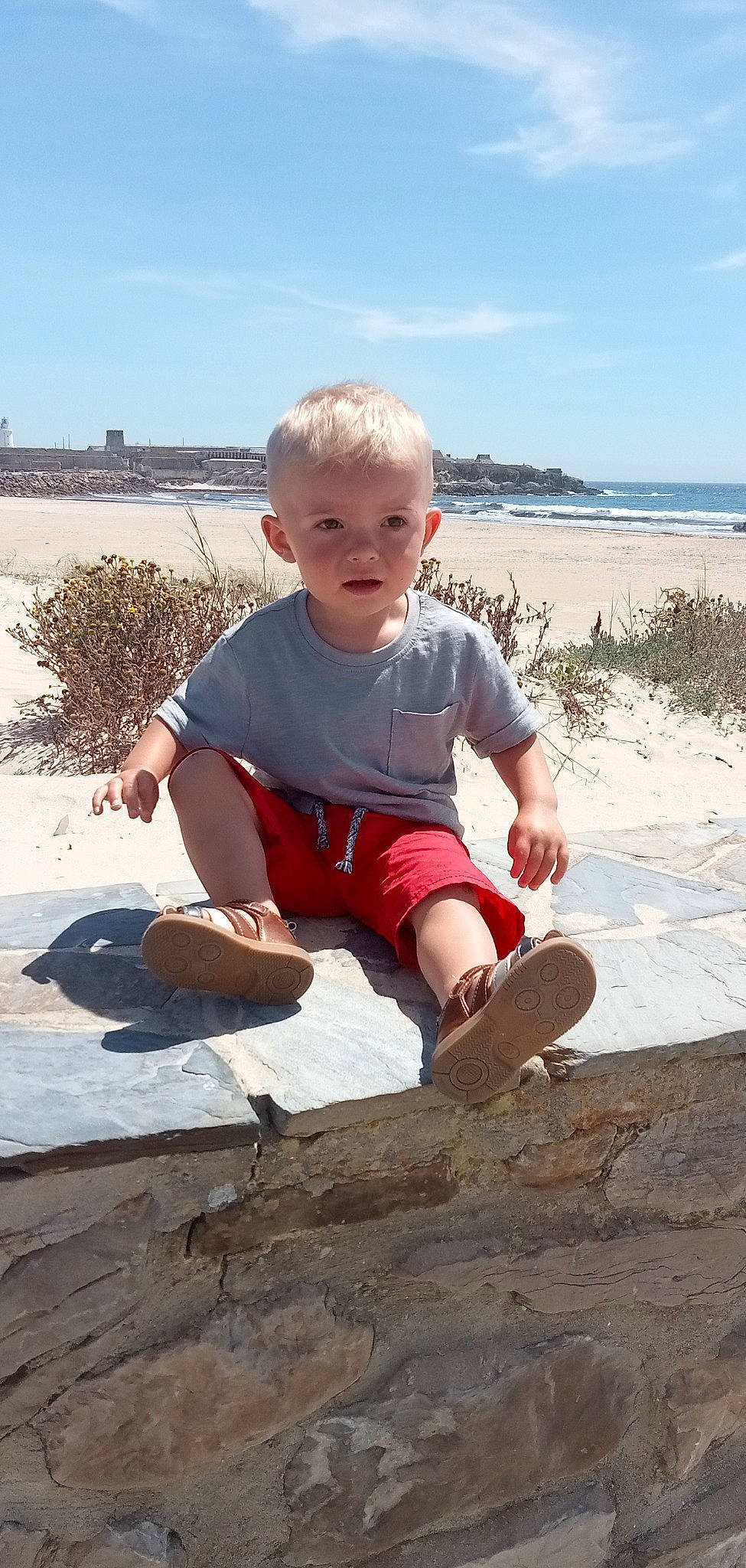 Nino participe au concours pour gagner de l'argent avec cette photo : barefoot, beach, cloud, foot, fun, landscape, leisure, people_in_nature, person, plant, rock, sand, shorts, sitting, sky, soil, t_shirt, thigh, toddler, travel