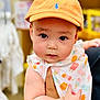baby, background_blur, cap, child, close_up, colorful_clothing, curious, cute, expression, face, hand, holding, indoor, infant, orange_cap, person, portrait, small_hand, soft_skin, young_child