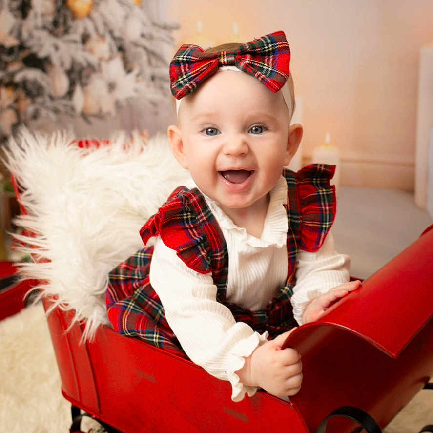 Ayla is registered to the contest to win money with this photo: baby, child, christmas_tree, cute, decorations, festive, fluffy_cushion, happy, holiday, holiday_decor, indoors, plaid, portrait, red_bow, red_dress, seasonal, sitting, sleigh, smiling, white_shirt