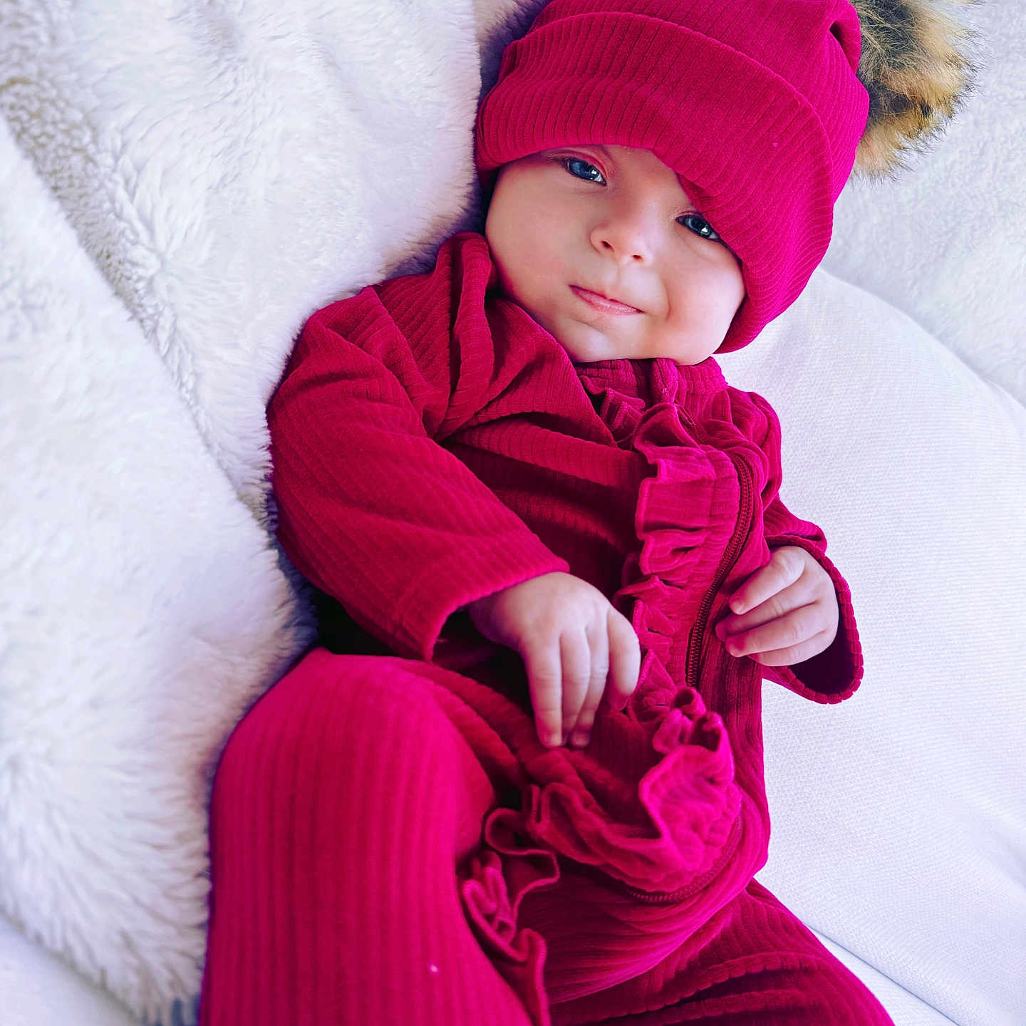 Aurora Elowen is registered to the contest to win money with this photo: baby, child, infant, magenta_clothing, hat, pom_pom, soft_blanket, white_background, smile, portrait, cute, cozy, indoor, relaxed, warm_clothing, fuzzy_texture, person, close_up, sitting, adorable