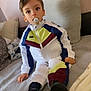 blanket, casual, child, clothing, couch, cozy, curious, face, footwear, home, indoors, pacifier, person, pillow, portrait, relaxed, sitting, soft_surface, tracksuit, young_child