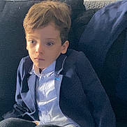 Isaak a rejoint le concours — aidez-le/la à gagner de superbes lots ! child, boy, sitting, indoor, couch, blazer, white_shirt, black_pants, thoughtful, young, hair, face, furniture, relaxed, casual, portrait, person, home, expression, seated