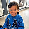 Isaak Menassel participe au concours pour gagner de l'argent avec cette photo : child, boy, smiling, blue_sweatshirt, indoor, window, natural_light, happy, portrait, casual_clothing, young_person, face, seated, home, floor, radiator, chair, hand, hair, eyes