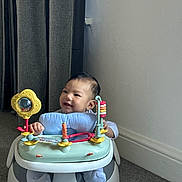 Ashton is registered to the contest to win money with this photo: baby, child, smiling, indoor, activity_seat, toy, play, carpet, wall, curtain, footwear, infant, person, cute, happy, seat, floor, head, face, clothing