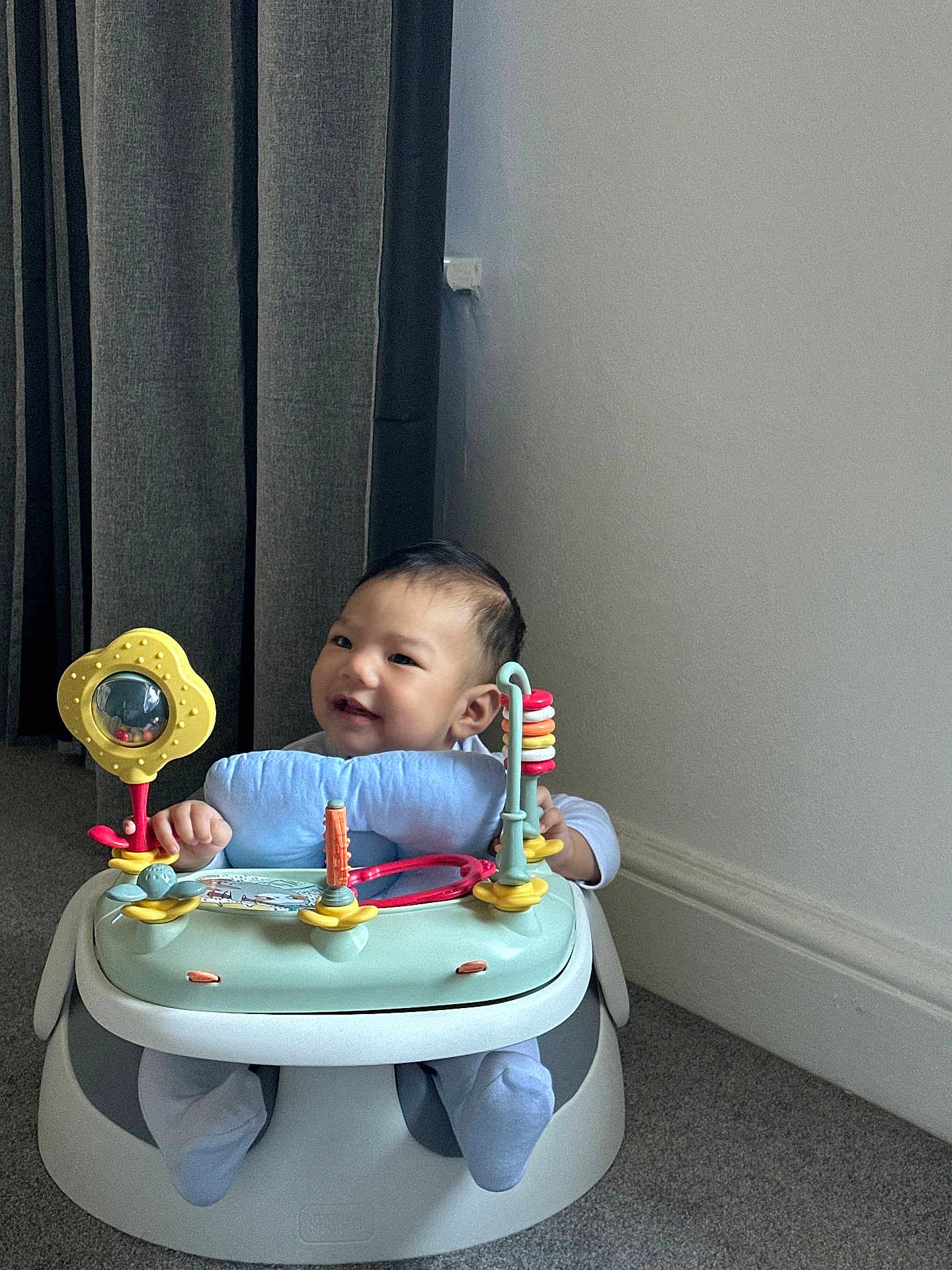 Ashton is registered to the contest to win money with this photo: baby, child, smiling, indoor, activity_seat, toy, play, carpet, wall, curtain, footwear, infant, person, cute, happy, seat, floor, head, face, clothing