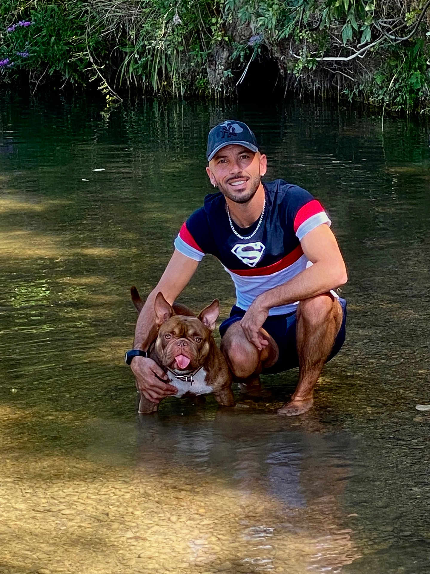 Ice participe au concours pour gagner de l'argent avec cette photo : man, dog, water, stream, nature, greenery, smiling, crouching, cap, shorts, outdoor, sunlight, reflection, pet, tongue_out, happy, casual_clothing, earrings, collar, shallow_water
