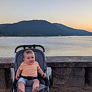 Tylio a rejoint le concours — aidez-le/la à gagner de superbes lots ! baby, casual_clothing, child, daylight, lake, mountains, nature, outdoor, peaceful, portrait, relaxing, scenic, sitting, sky, stone_railing, stroller, sunset, travel, vacation, water