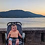 baby, casual_clothing, child, daylight, lake, mountains, nature, outdoor, peaceful, portrait, relaxing, scenic, sitting, sky, stone_railing, stroller, sunset, travel, vacation, water