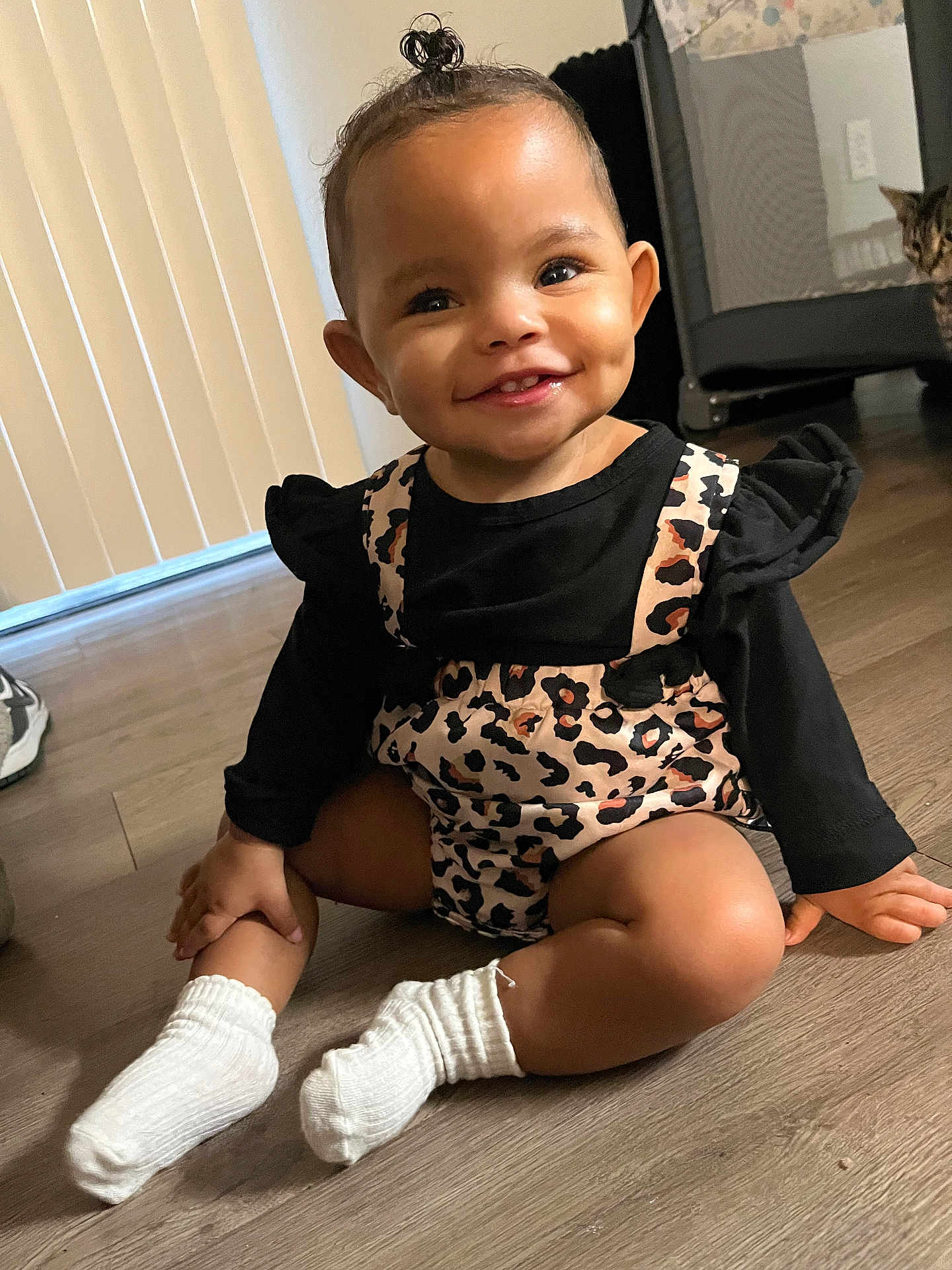 Eleia joined the competition — help win amazing prizes! toddler, child, smile, sitting, leopard_print, outfit, white_socks, floor, wooden_floor, indoor, topknot, happy, cat, pet, curious, background, person, baby, cute, portrait
