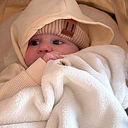 Eden a rejoint le concours — aidez-le/la à gagner de superbes lots ! baby, infant, blanket, hat, hoodie, knit_hat, beige, cream, soft_texture, cozy, wrapped, cute, child, face, portrait, warm_clothing, indoor, comfort, sleepy, snuggled