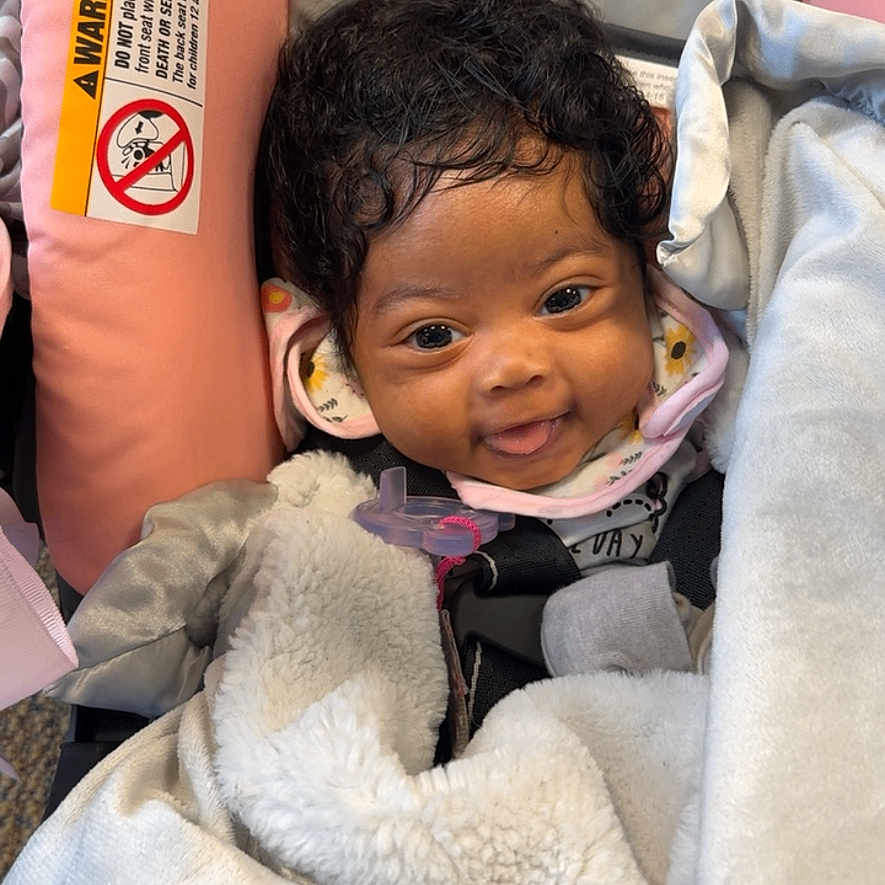 Zaraya joined the competition — help win amazing prizes! baby, blanket, car_seat, child, clothing, cozy, curly_hair, cushion, cute, face, happy, indoors, infant, person, portrait, safety_warning, seatbelt, smiling, wrapped, young_child