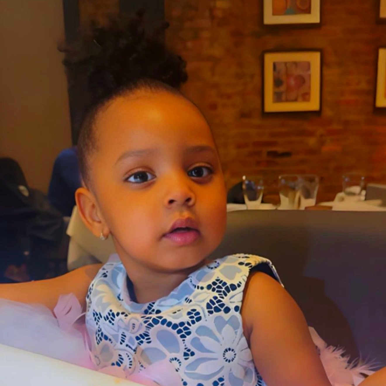 Cherifah joined the competition — help win amazing prizes! artwork, brick_wall, child, curly_hair, cute, dress, earrings, face, girl, glass, hair, indoor, looking_away, patterned_clothing, portrait, restaurant, seated, skin, table, toddler