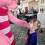 child, girl, mascot, pink, smile, happy, restaurant, indoor, carpet, people, table, chair, costume, interaction, fun, celebration, curly_hair, casual_clothing, light, decor