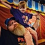 child, man, beard, glasses, cap, tshirt, carnival, background, colorful, holding, shoulders, smile, happy, indoor, celebration, family, fun, person, light, bench