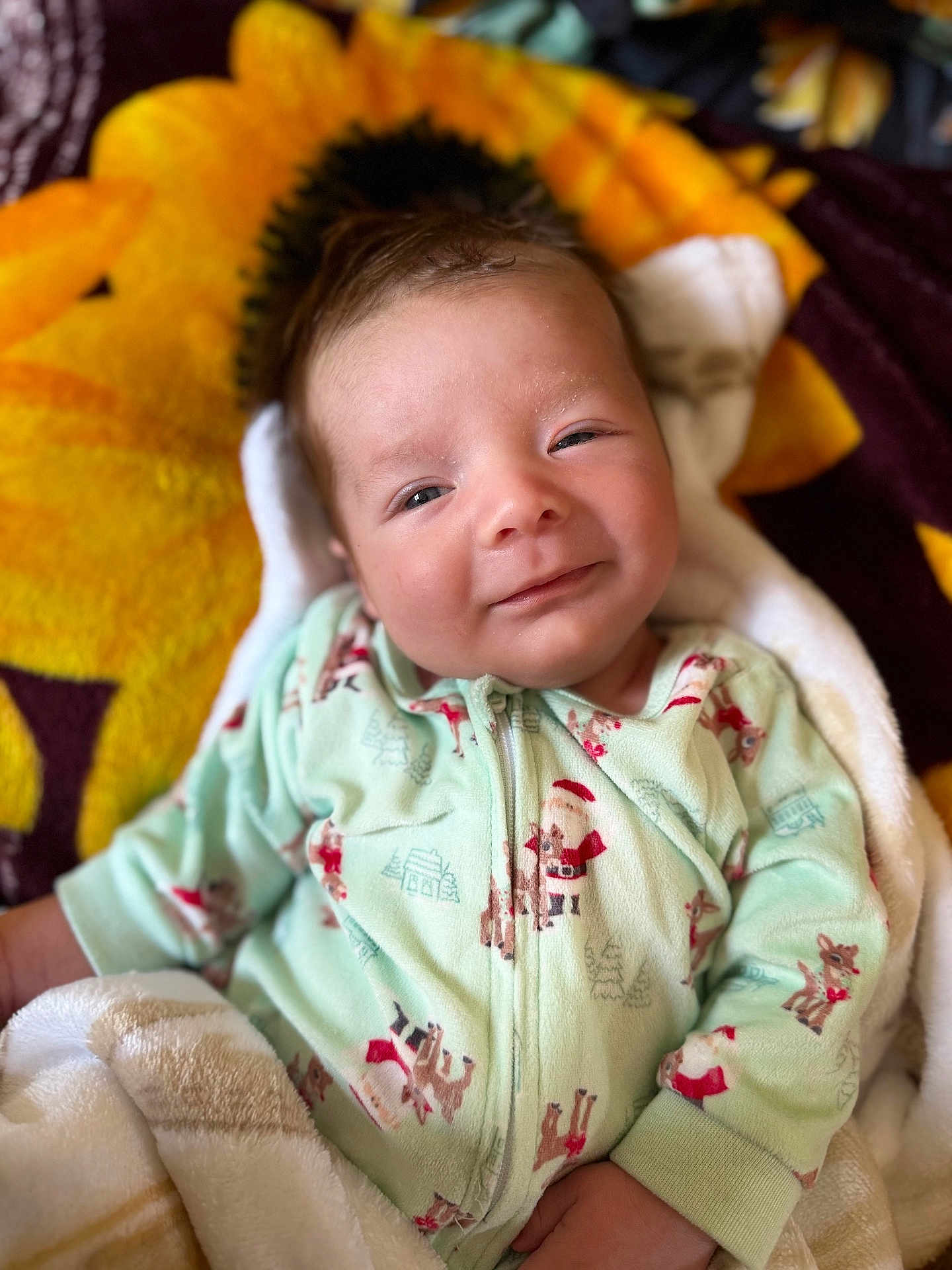 Rylan is registered to the contest to win money with this photo: baby, blanket, child, clothing, cozy, cute, face, green, happy, indoors, infant, onesie, pattern, portrait, resting, smile, soft, sunflower, yellow, young
