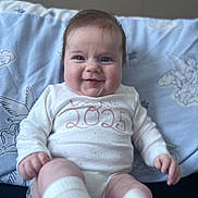 Delilah-Mae is registered to the contest to win money with this photo: baby, infant, smiling, onesie, white_clothing, socks, chubby_cheeks, face, person, indoor, blanket, patterned_blanket, blue_background, happy, cute, child, soft_lighting, portrait, seated, young