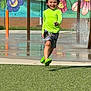 child, running, smiling, neon_green, shirt, shorts, green_crocs, water_splash, mural, flowers, cats, playground, grass, daylight, outdoor, happy, person, fun, sprinkler, colorful