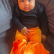 Alanni is registered to the contest to win money with this photo: baby, child, infant, black_clothing, orange_pants, velvet, ruffles, braided_hair, beads, sitting, couch, indoor, cute, portrait, face, hands, feet, curious, soft_lighting, young