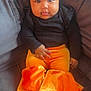baby, child, infant, black_clothing, orange_pants, velvet, ruffles, braided_hair, beads, sitting, couch, indoor, cute, portrait, face, hands, feet, curious, soft_lighting, young