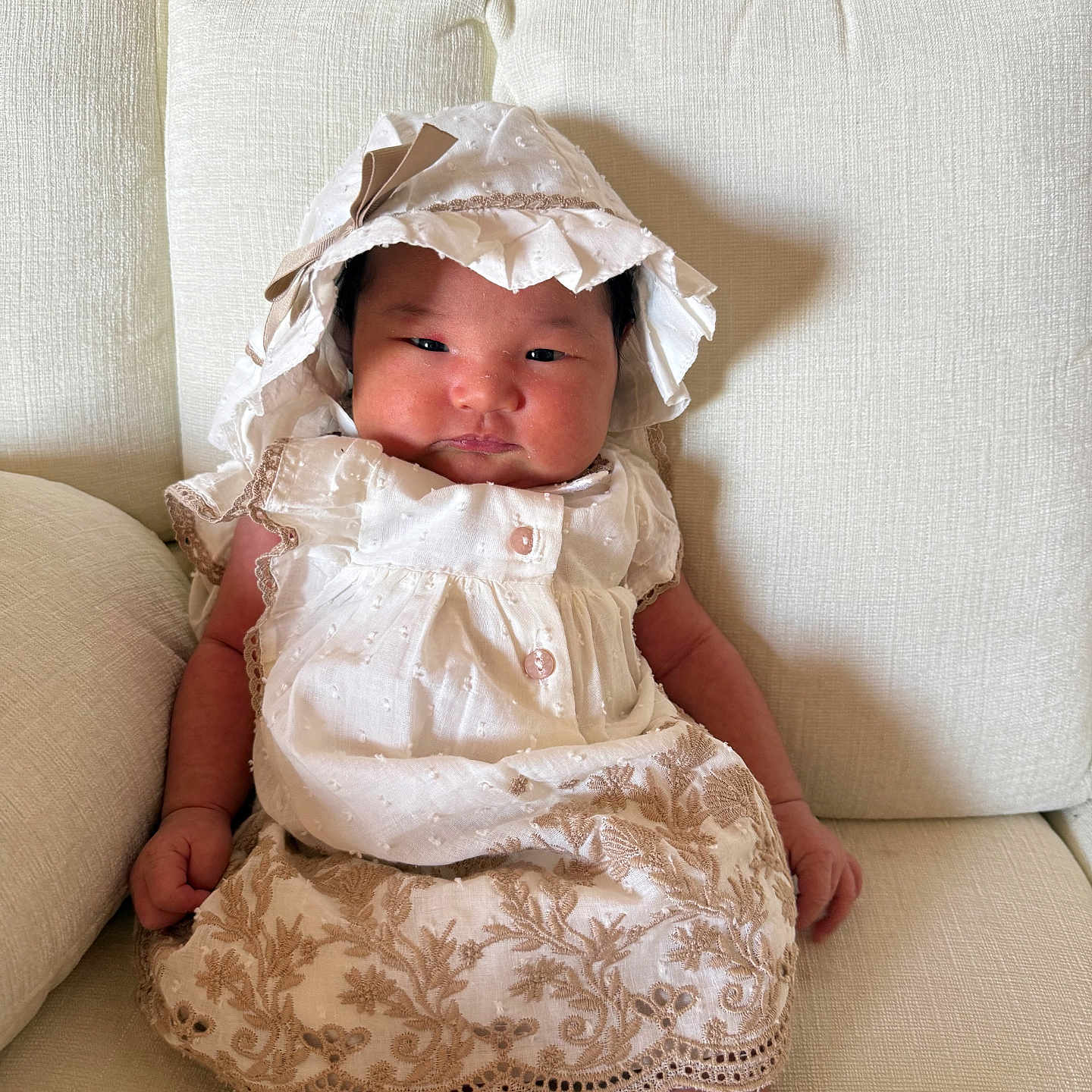 Ener joined the competition — help win amazing prizes! baby, infant, child, portrait, sitting, sofa, couch, bonnet, dress, embroidered_clothing, white_clothing, cream_color, indoors, furniture, face, hands, legs, relaxed, fashion, photography