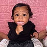 adult_legs, baby, black_clothing, black_pants, butterfly_pattern, carpet, child, curly_hair, cute, foot, hand, indoor, infant, pacifier, person, pink_wall, sitting, textured_wall, toddler, wide_eyes