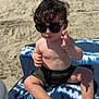 child, toddler, beach, sunglasses, sand, towel, sunlight, barefoot, curly_hair, summer, outdoor, casual_clothing, bracelet, relaxed, sitting, shadow, skin, foot, nature, vacation