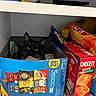 cat, box, snacks, chips, pantry, shelf, black_and_white_cat, curious, indoor, food, packaging, lay's, cheez_it, doritos, fritos, cereal_box, pet, animal, cute, looking