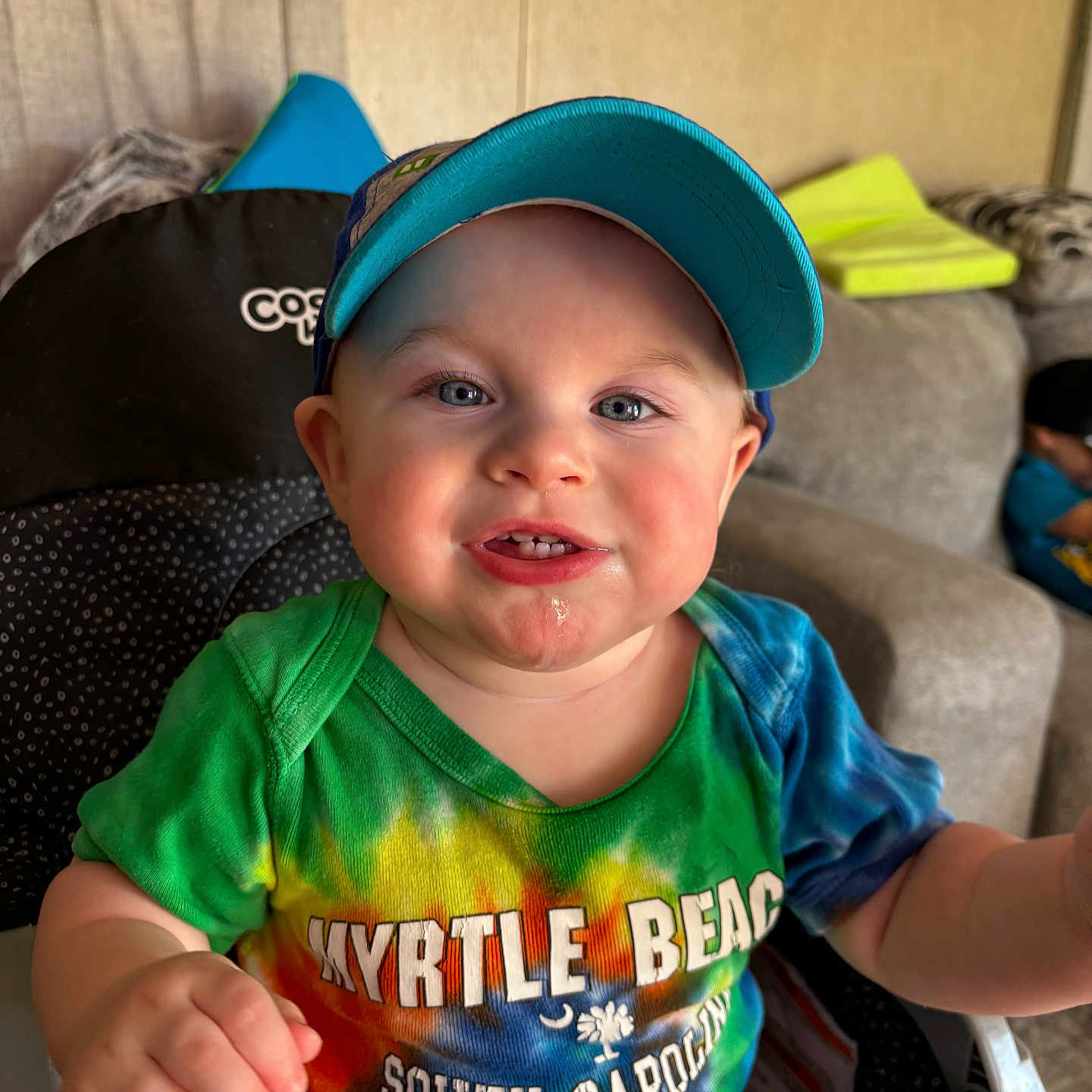 Journey joined the competition — help win amazing prizes! toddler, child, baby, cap, tie_dye_shirt, smiling, drool, high_chair, indoor, couch, living_room, person, face, blue_eyes, colorful_clothing, furniture, seated, happy, closeup, casual