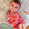 baby, child, smiling, pink_clothing, orange_flower_pattern, onesie, quilted_mat, toy, indoor, floor, cute, happy, infant, person, portrait, playtime, soft_toys, head, eyes, skin
