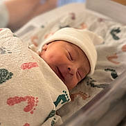 Elias is registered to the contest to win money with this photo: baby, baby_clothes, bassinet, blanket, closeup, cozy, cute, face, footprint_pattern, hat, hospital, indoors, infant, newborn, peaceful, portrait, resting, sleeping, soft_light, wrapped