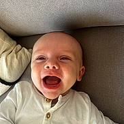 Eden a rejoint le concours — aidez-le/la à gagner de superbes lots ! baby, infant, smiling, happy, face, person, white_clothing, buttoned_shirt, couch, fabric, texture, indoor, child, portrait, head, skin, eyes, mouth, cute, lying_down