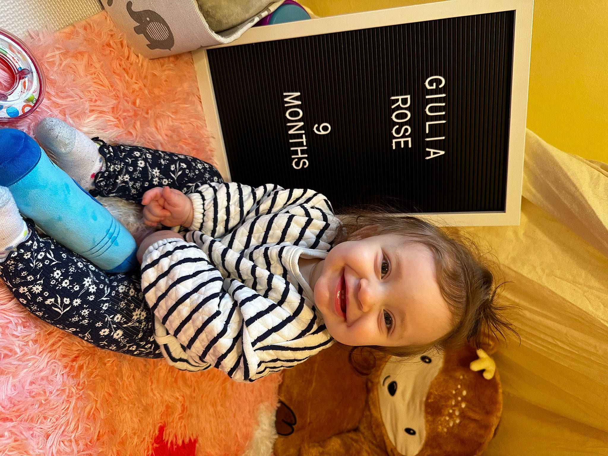 Giulia is registered to the contest to win money with this photo: baby_toddler_clothing, child, cool, flooring, fun, happy, human_leg, joy, pattern, person, plant, play, room, sitting, sleeve, smile, snapshot, t_shirt, thigh, toddler