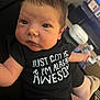 baby, infant, onesie, black_clothing, face, eyes, arm, hand, indoor, living_room, television, furniture, person, cute, newborn, skin, expression, sitting, home, relaxed