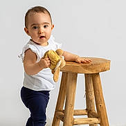 Giuseppa a rejoint le concours — aidez-le/la à gagner de superbes lots ! baby, child, curious_expression, cute, face, fluffy_rug, furniture, hand, indoors, minimalist_background, navy_pants, person, plush_toy, portrait, standing, studio_light, toddler, white_top, wooden_stool, young_child