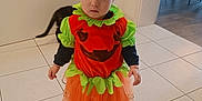 Giuseppa a rejoint le concours — aidez-le/la à gagner de superbes lots ! baby, black_cat, cat, child, costume, curious, cute, dress, floor, green, halloween, holiday, indoor, orange, person, pumpkin, shoes, standing, tile_floor, toddler