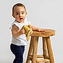 Giuseppa participe au concours pour gagner de l'argent avec cette photo : baby, child, curious_expression, cute, face, fluffy_rug, furniture, hand, indoors, minimalist_background, navy_pants, person, plush_toy, portrait, standing, studio_light, toddler, white_top, wooden_stool, young_child