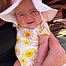 baby, child, smiling, sun_hat, onesie, sun_pattern, adult_hand, outdoor, sunlight, cute, happy, face, arm, person, holding, red_metal, background, warm, skin, infant