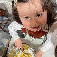 Tania a rejoint le concours — aidez-le/la à gagner de superbes lots ! child, mixing, bowl, whisk, kitchen, happy, smile, brown_hair, hair_clip, apron, long_sleeve, countertop, tile_floor, wooden_chair, cooking, baking, closeup, face, person, indoors