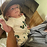 Ryker joined the competition — help win amazing prizes! baby, child, hat, cactus_print, clothing, indoor, person, holding, adult, arm, face, curious, seated, shirt, adidas, couch, furniture, wood_paneling, cozy, home