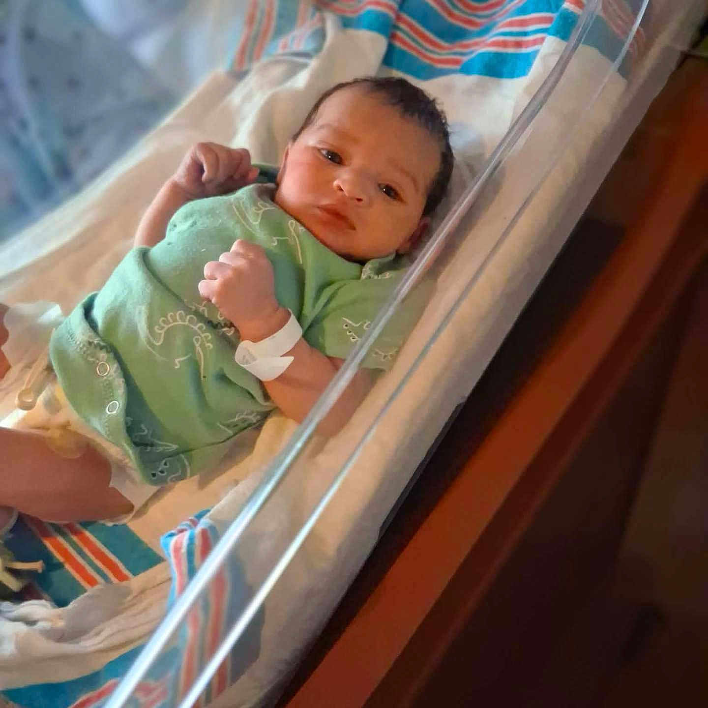 Zaire is registered to the contest to win money with this photo: newborn, baby, hospital, bassinet, onesie, wristband, blanket, striped_blanket, infant, sleeping_area, medical, person, cute, indoor, healthcare, resting, small, face, child, newborn_baby