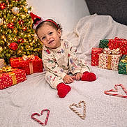 Kenzi a rejoint le concours — aidez-le/la à gagner de superbes lots ! blanket, candy_cane, celebration, child, christmas_lights, christmas_tree, cozy, cute, festive, gift_wrap, heart_shape, holiday, holiday_decor, indoors, pajamas, presents, red_socks, santa_hat, smiling, toddler