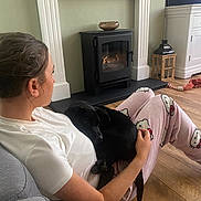 Milo joined the competition — help win amazing prizes! person, dog, puppy, indoor, pajamas, hello_kitty, fireplace, wood_floor, couch, television, relaxing, home, pet, black_dog, sitting, casual, hand, comfort, wooden_lantern, living_room