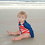 Westen is registered to the contest to win money with this photo: toddler, child, beach, sand, water, waves, swimsuit, red, white, blue, sitting, barefoot, serious, young_child, outdoor, summer, ocean, coast, nature, person